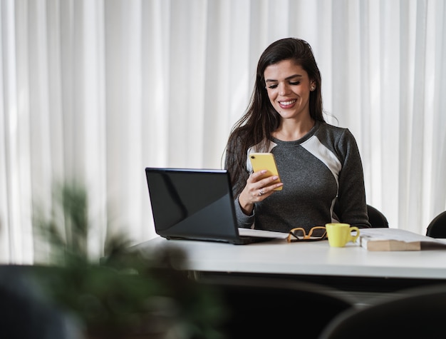 Junge schöne Brasilianerin, die Smartphone benutzt und mit Laptop arbeitet