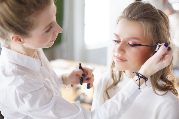 Junge schöne Braut, die Hochzeitsmake-up durch professionellen Maskenbildner anwendet