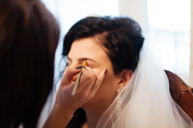 Junge schöne Braut, die Hochzeitsschminke durch Maskenbildner anwendet