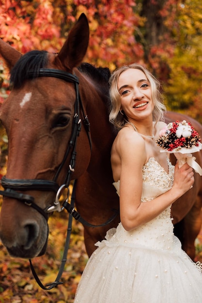 Junge schöne Braut in einem üppigen weißen Kleid glückliche Spaziergänge mit einem Pferd im Herbstwald