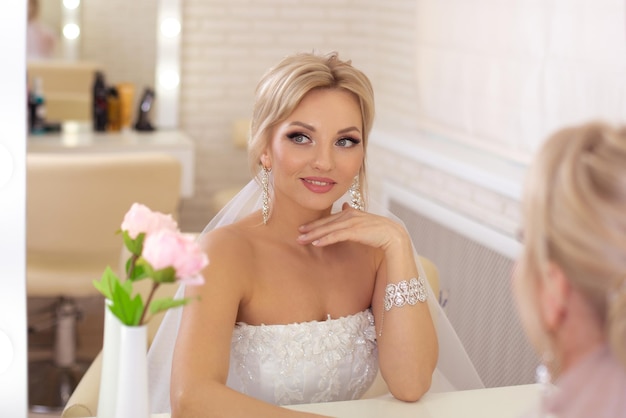 Junge schöne Braut mit blonder Hochzeitsfrisur und Make-up im Friseursalon