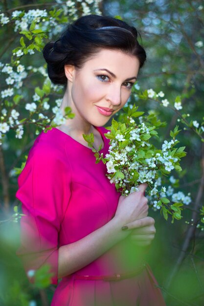 Junge schöne brünette Frau im rosa Kleid im blühenden Kirschbaumgarten