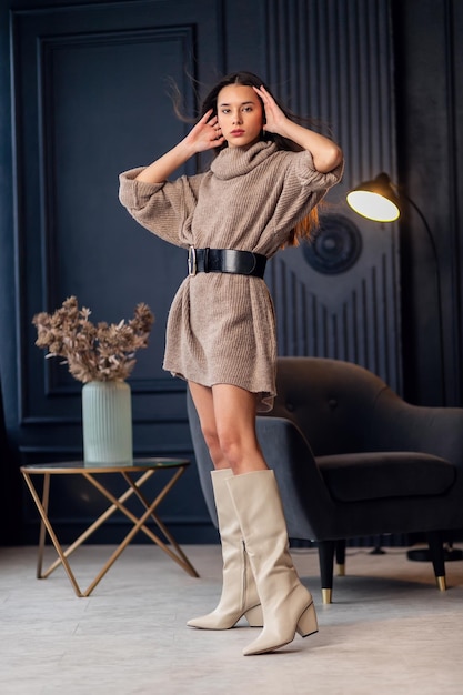 Junge schöne Brünette Frau in beige Stiefeln in einem schönen Innenraum Porträt in voller Länge Junge elegante Frau mit beige stilvollem Look Hübsches Mädchen mit langen brünetten gewellten Haaren Modische Dame