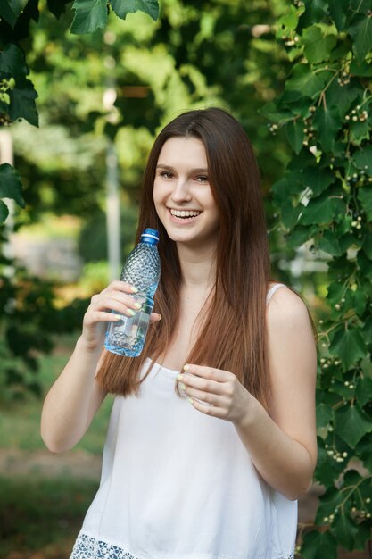 junge schöne brünette frau trinkt wasser aus der flasche in einem park