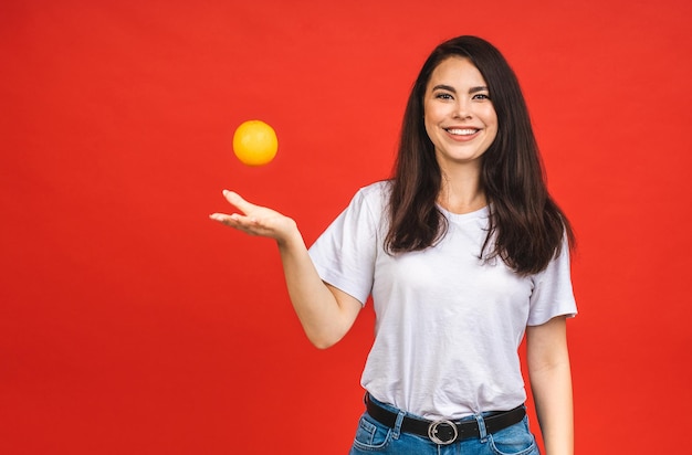 Junge schöne Brunettefrau, die orange Frucht lokalisiert über rotem Hintergrund hält