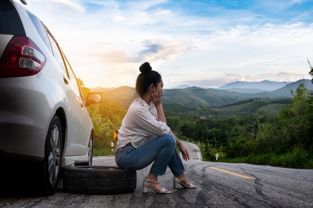 Junge schöne Dame sitzt in der Nähe des Autos, um auf der öffentlichen Straße um Hilfe zu rufen