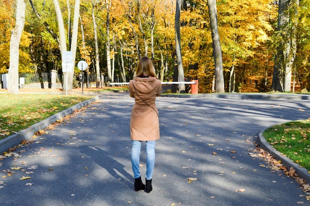 Junge schöne dünne schlanke Mädchen eine Frau in einem braunen Mantel mit langen Haaren geht im Herbstpark spazieren