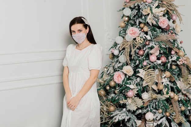 Junge schöne europäische Frau in medizinischer Maske mit Weihnachtsgeschenken zu Hause, Quarantäne-Coronavirus.