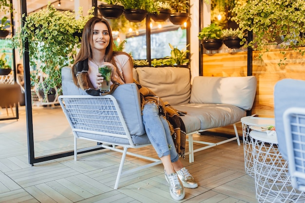 Junge schöne Frau auf einer Sommerterrasse in Freizeitkleidung trinkt Cocktail. Mit einer Decke bedeckt