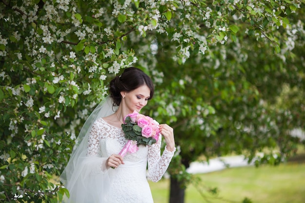 Junge schöne frau, braut mit rosa hochzeitsstrauß im blühenden garten