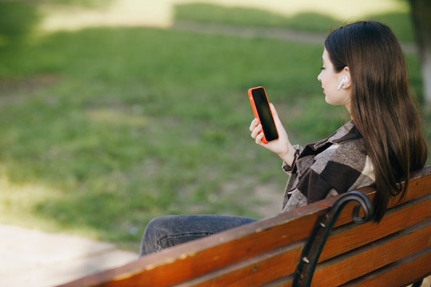 Junge schöne Frau, die auf einer Bank mit dem Telefon steht