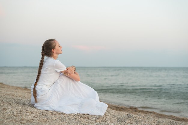 Junge schöne Frau, die auf Sandstrand gegen Meer und Träume sitzt.