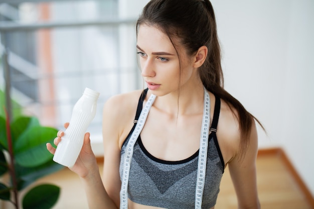 Junge schöne Frau, die aus einer Plastikflasche Joghurt trinkt.