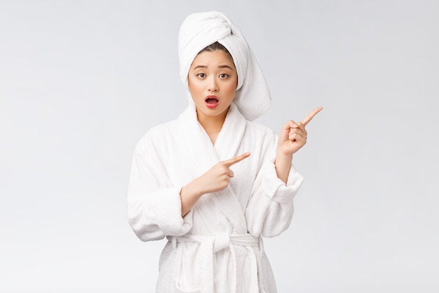 Junge schöne Frau, die Duschtuch nach Bad über isolierter weißer Wand trägt, die mit Finger zeigt.