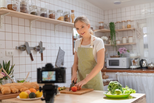 Junge schöne Frau, die ein Kameraaufnahmevideo verwendet, wie man einen Salat macht und eine Bäckerei für die Veröffentlichung in sozialen Medien in ihrem Kanal macht Essen gesund zu Hause Küche