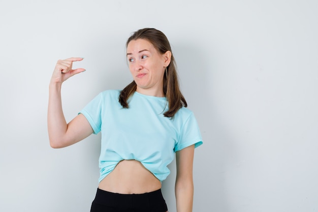 Junge schöne Frau, die ein kleines Schild zeigt, im T-Shirt beiseite schaut und verwirrt aussieht. Vorderansicht.