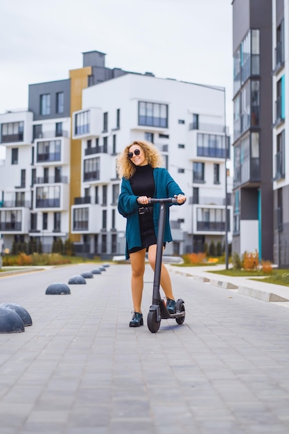 Foto junge schöne frau, die einen elektroroller zur arbeit reitet, modernes mädchen, neue generation, elektrischer transport, ökologie, ökologischer transport, sonnenuntergang