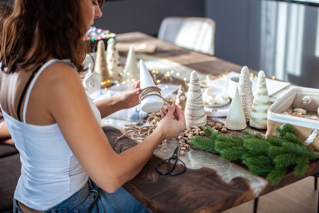 Junge schöne Frau, die einen Schaumkegel mit Schnurgarn einwickelt und Weihnachtsbaum bastelt