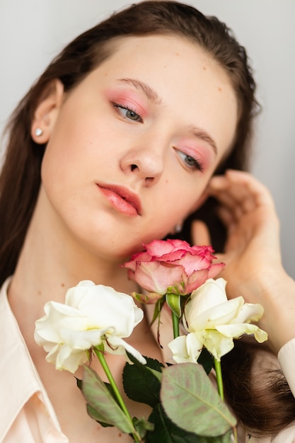 Junge schöne Frau, die einen Strauß roter Rosen riecht. Modeinnenfoto einer schönen lächelnden Frau mit dunklem Haar, die am Valentinstag einen großen Strauß roter Rosen hält