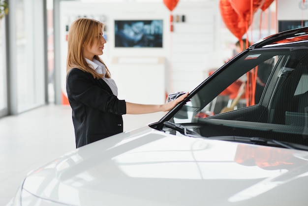 Junge schöne frau, die ihre liebe zu einem auto in einem autohaus zeigt