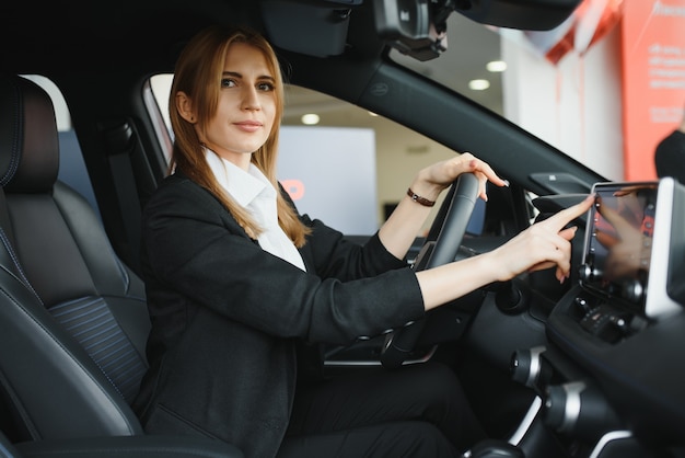 Junge schöne Frau, die ihre Liebe zu einem Auto in einem Autohaus zeigt