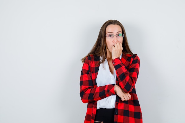 Junge schöne Frau, die ihre Nägel in lässigem Outfit beißt und gestresst aussieht, Vorderansicht.