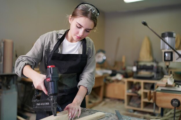 Junge schöne Frau, die im Tischler-DIY-Werkstattraum arbeitet. Kleinunternehmer, junge Frau, die in der Möbelfabrik arbeitet.