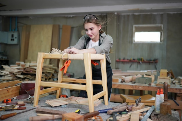 Junge schöne Frau, die im Tischler-DIY-Werkstattraum arbeitet. Kleinunternehmer, junge Frau, die in der Möbelfabrik arbeitet.