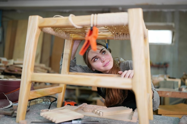 Junge schöne Frau, die im Tischler-DIY-Werkstattraum arbeitet. Kleinunternehmer, junge Frau, die in der Möbelfabrik arbeitet.