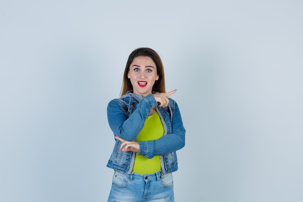 Junge schöne Frau, die in Denim-Outfit in entgegengesetzte Richtungen zeigt und glücklich aussieht. Vorderansicht.