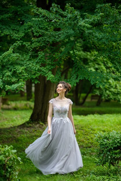 Junge schöne Frau, die in einem blauen Kleid im Park aufwirft.