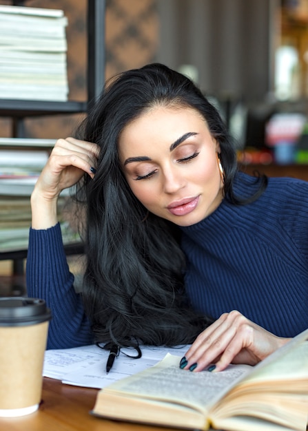 Junge schöne Frau, die interessantes Buch im Café liest.