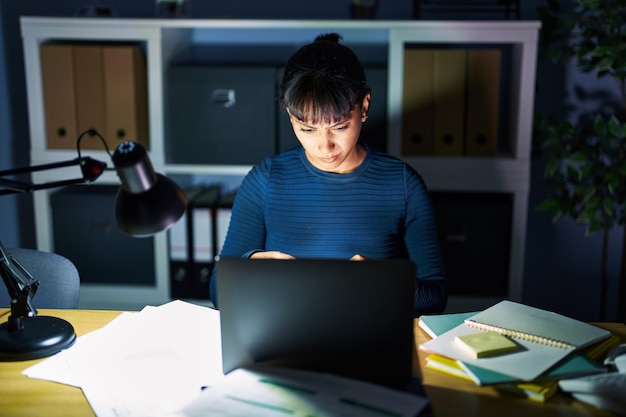 Junge schöne Frau, die nachts im Büro arbeitet, ist skeptisch und nervös und runzelt die Stirn wegen des Problems. negativer Mensch.