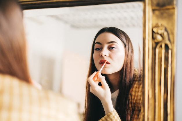 Junge schöne Frau, die Spiegel beim Schminken betrachtet, Lippenstift anwendend.