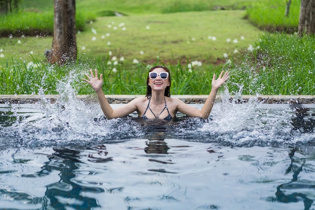 junge schöne Frau, die Wasser im Swimmingpool spritzt