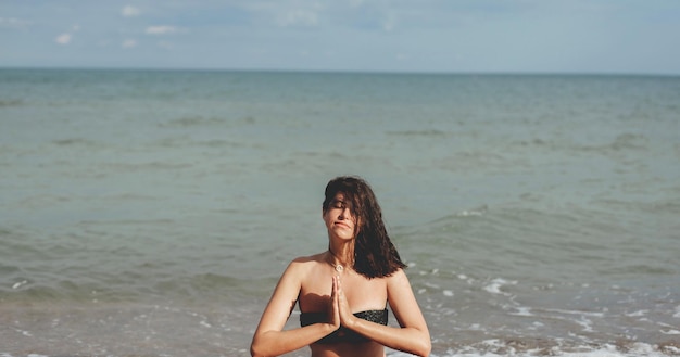 Junge schöne Frau, die Yoga am Strand praktiziert, sitzt auf Sand und meditiert Psychische Gesundheit und Selbstpflegekonzept Glückliches Mädchen, das sich im Sommerurlaub an der Küste entspannt