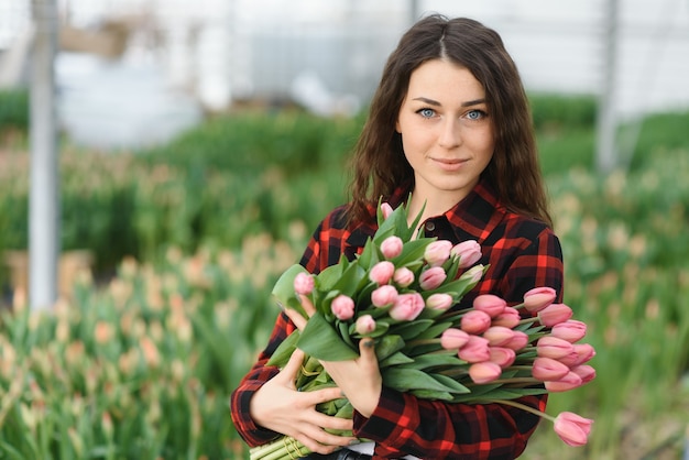 Junge schöne Frau Gewächshausarbeiter hält eine blühende Tulpe in ihren Händen und lächelt.