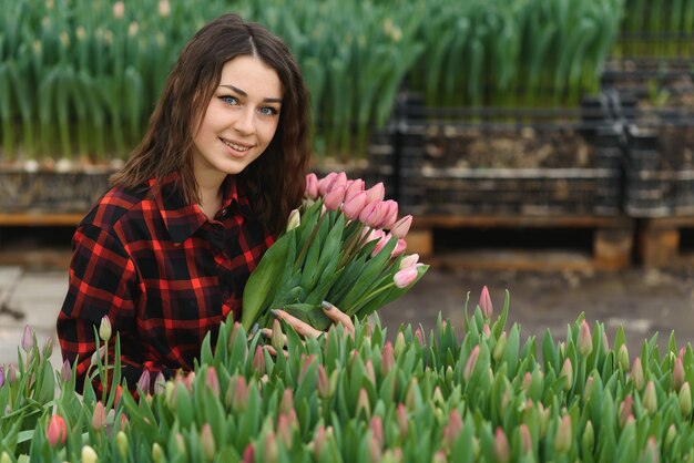 Junge schöne Frau Gewächshausarbeiter hält eine blühende Tulpe in ihren Händen und lächelt.