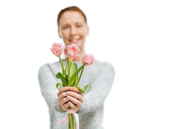 Junge schöne Frau grauer Pullover gibt rosa Tulpen auf weißem Hintergrund. Unschärfeporträt, selektiver Fokus.