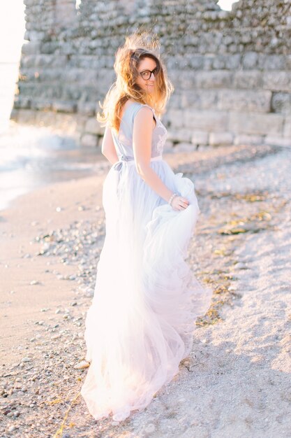 Junge schöne Frau im blauen eleganten Kleid, das nahe dem See Gardasee und der Festung in Sirmione, Italien geht. Schöner Spaziergang in Sirmione