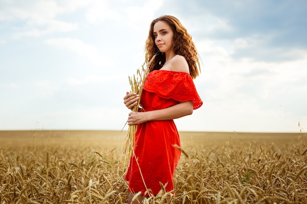 Junge schöne Frau im goldenen Weizenfeld glückliche Frau im roten Kleid, die das Leben in der Feldnatur genießt...