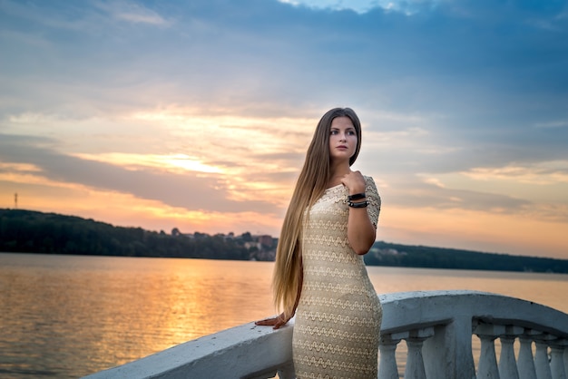 Junge schöne Frau im Kleid, das an der Seeküste bei Sonnenuntergang aufwirft