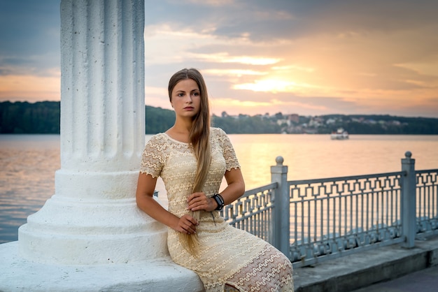 Junge schöne Frau im Kleid, das an der Seeküste bei Sonnenuntergang aufwirft