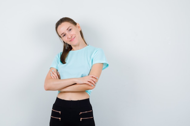 Junge schöne Frau im T-Shirt, Hose mit verschränkten Armen und fröhlichem Blick, Vorderansicht.