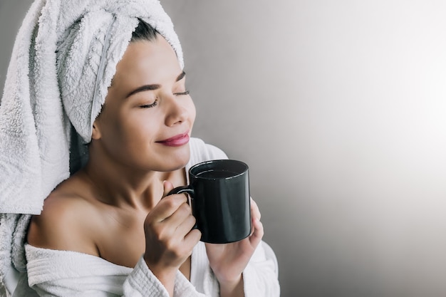 Junge schöne Frau im weißen Handtuch und im Gewand, die Kaffee trinken