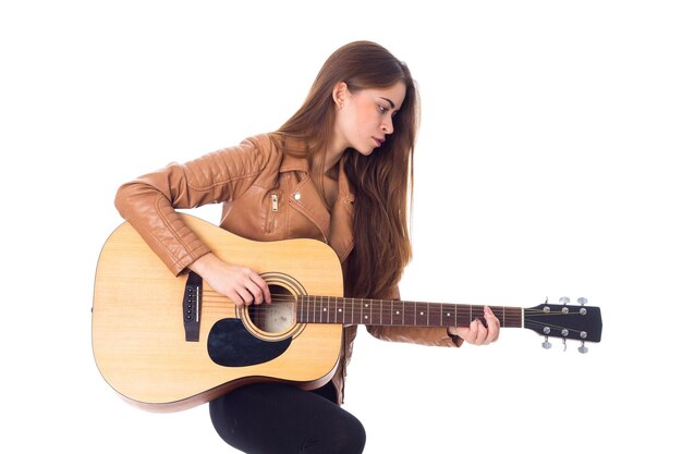 Junge schöne Frau in brauner Jacke und schwarzer Hose, die eine Gitarre hält und ihr Haar repariert