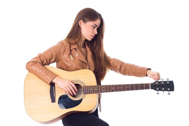 Junge schöne Frau in brauner Jacke und schwarzer Hose, die eine Gitarre hält und ihr Haar repariert