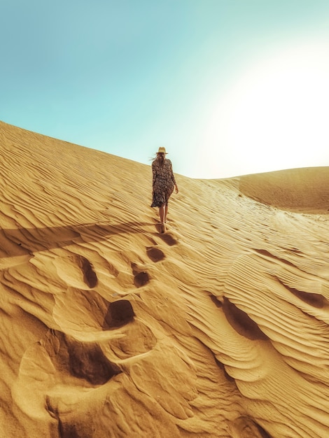 Junge schöne Frau in einem langen Kleid geht entlang die Sanddünen der Dubai-Wüste