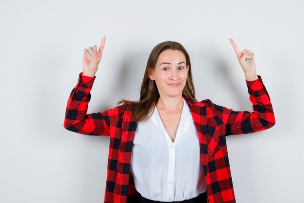 Foto junge schöne frau in lässigem outfit, die nach oben zeigt und fröhlich aussieht, vorderansicht.