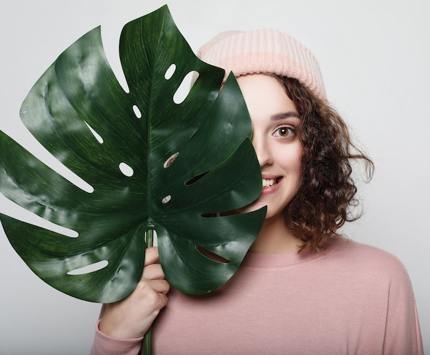 Junge schöne Frau in rosa Freizeitkleidung mit Monstera-Blatt posiert auf weißem Hintergrund